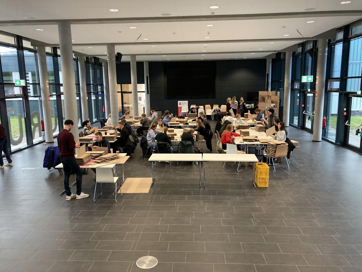 Weitwinkelaufnahme des Saals mit Arbeitstischen und Studierenden beim Modellbau.