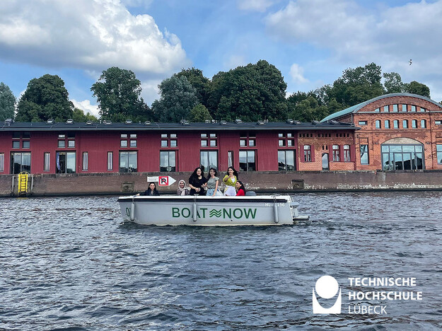 Boot mit Studierenden im Fluss und im Hintergrund Häuserreihe