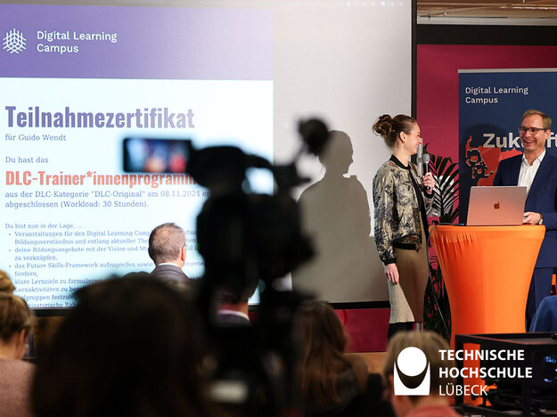 Lübecks Staatssekretär erster Nutzer der Digital Learning Plattform Zwei Personen stehen vorne am Rednerpult