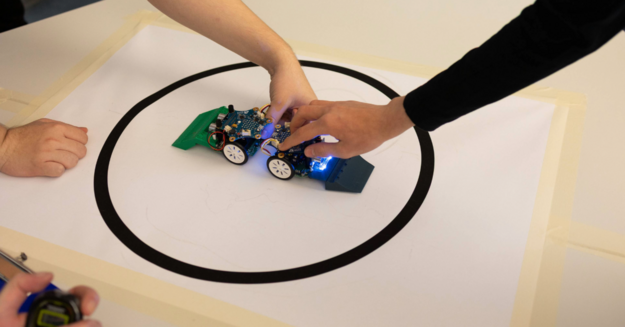 Auf dem Bild sieht man zwei Hände, wie sie zwei Roboter gegeneinander antreten lassen