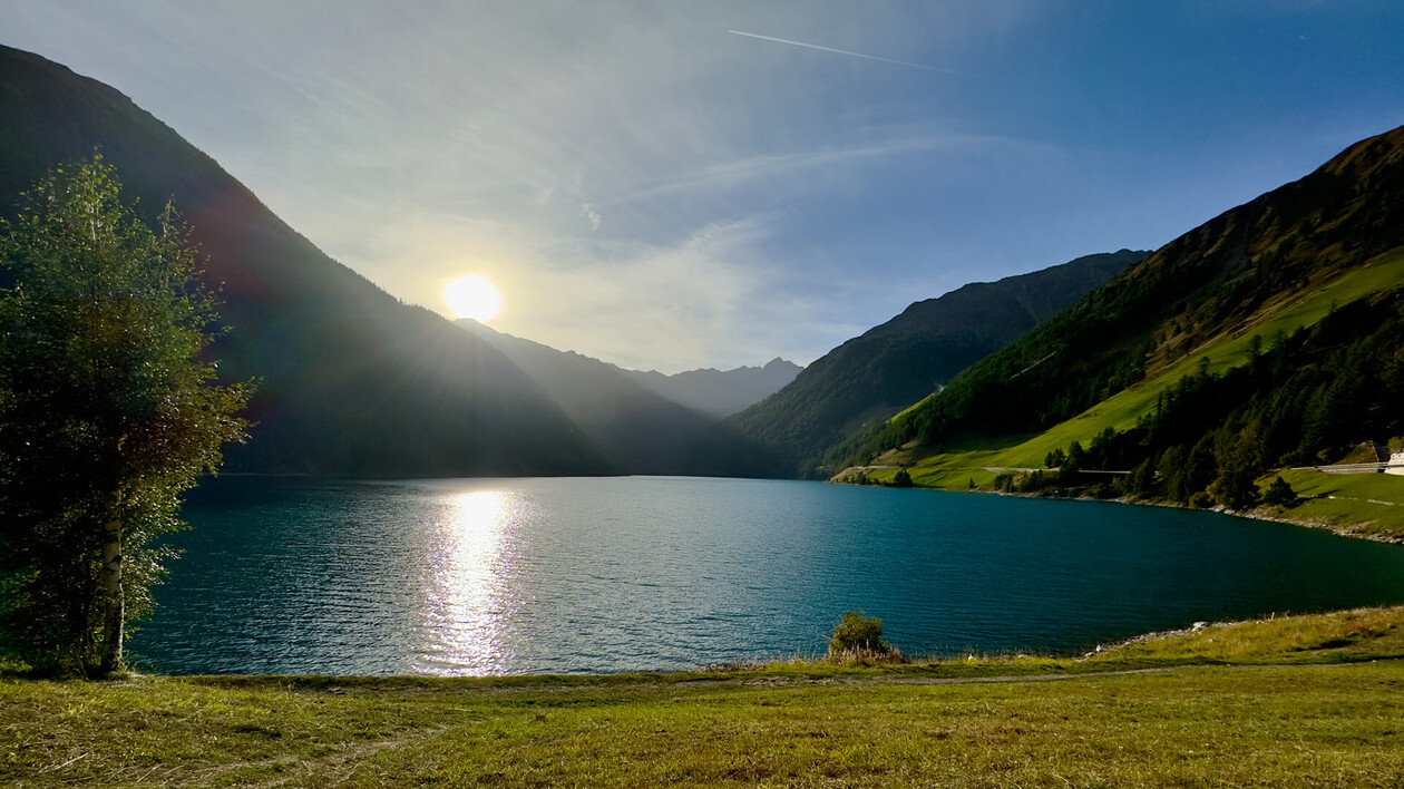 A clear blue mountain lake at sunset, surrounded by green and forested slopes.