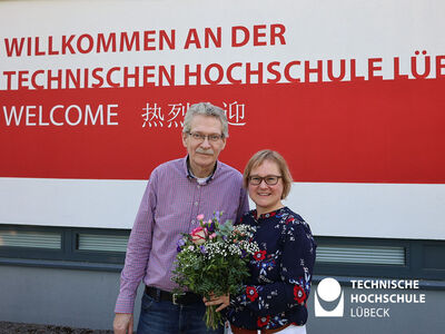 TH Lübeck Präsidentin steht mit Blumenstrauß neben Senatsvorsitzenden