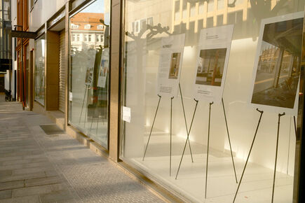 Ausstellung in leerstehendem Ladenlokal in der Innenstadt: Mehrere Stellwände mit Poster-Präsentationen auf Staffeleien hinter einer Glasfront, beleuchtet von warmem Abendlicht – Projekt zur Zwischennutzung von Leerstand im Stadtgebiet