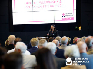 Frau steht am Rednerpult und im Hintergrund eine Präsentation