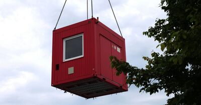 Der rote Container in der Luft, rechts im Bild ein Baum