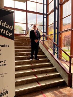 A man in a suit stands on a wide staircase inside a modern building.