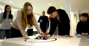 Jugendliche und ein Betreuer beobachten gespannt einen Roboter auf dem Tisch.