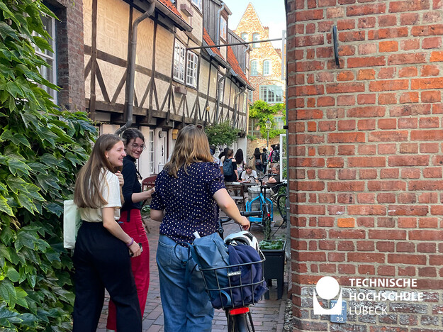 Studierende gehen durch eine schmale Häusergasse