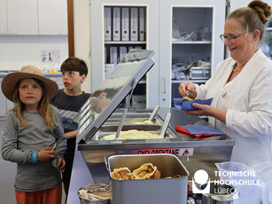 Kühle Erfrischung für die Gäste zwei Kinder stehen hinter einer Theke, eine Frau presst eine Kugel Eis in eine Waffel