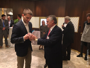 Two men in business attire shake hands during an awards presentation at a reception.