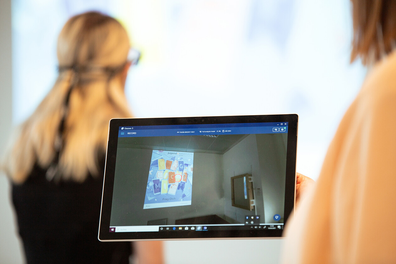 Eine Person hält ein Tablet, das eine Videoaufzeichnung einer Präsentation zeigt.