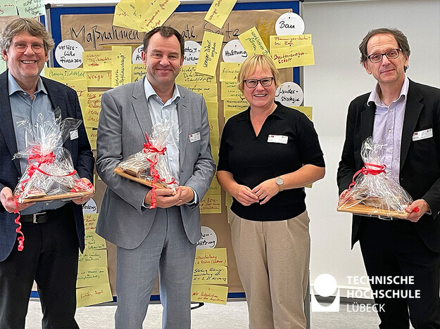 TH Lübeck Kanzlerin dankt den Referenten Kanzlerin und drei Referenten mit Geschenk in den Händen stehen vor Pinnwand