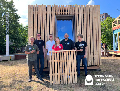 Ausstellung vor den Deichtorhallen Hamburgs 6 Personen stehen vor dem Holzhaus und eine daovn hält ein Holzpanel
