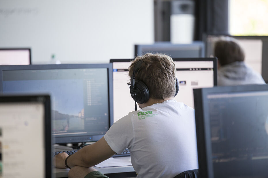 Ein Studierender sitzt vor einem Rechner und arbeitet an einer virtuellen Welt.