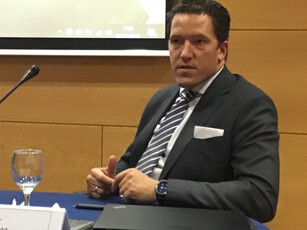 A man in a suit with a striped tie speaks during a conference panel.