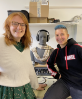 Zwei Hörakustik-Studentinnen im Labor der TH Lübeck neben einem Kunstkopf mit Kopfhörern für audiologische Messungen.