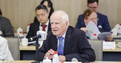 Mann im Anzug sitzt an einem Konferenztisch mit Namensschild „Hans Wilhelm Orth“, Mikrofon und Unterlagen vor sich, weitere Personen im Hintergrund.