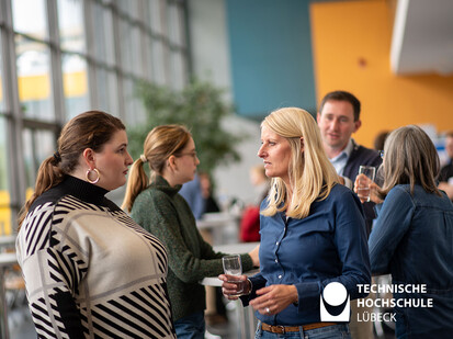 Austausch in der Pause Eine Gruppe Frauen steht zusammen und spricht miteinander. Sie sind alle in einem Raum, der mit vielen Stehtischen ausgestattet ist. Die Frauen scheinen zu genießen, wie sie miteinander plaudern und trinken.