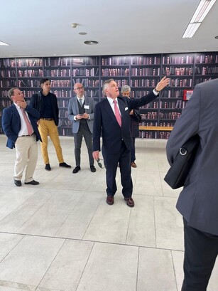 A man gestures towards a large wall graphic of a bookshelf in a library.