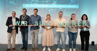 Gruppe auf Bühne hält große Buchstaben: "WIR SIND HOEREN".