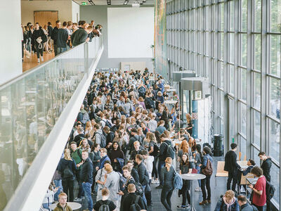Man sieht viele junge Menschen in einem Foyer, die sich über Studienangebote informieren