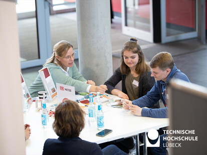 4 Personen sitzen an einem Tisch und eine zeigt mit einem Kugelschreiber auf etwas