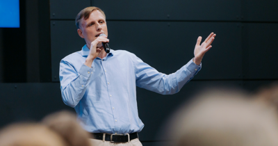 Ein Mann in blauem Hemd mit Mikro spricht zu einer Menschenmenge