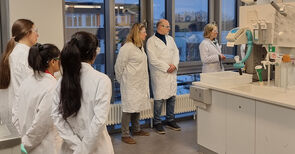 Sechs Personen in weißem Kittel laufen durch ein Labor