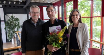 Drei Personen stehen nebeneinander, einer hält einen Blumenstrauß.