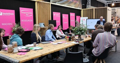An einem Messestand sitzen einige Personen um einen Tisch zusammen.