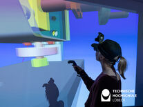 Frau mit AR Brille und Joystick steht vor einer Leinwand