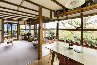 Heller Wohnraum mit Holzrahmenbau, großen Fenstern und vielen Pflanzen.