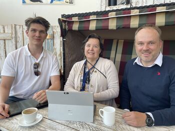 Drei Personen sitzen lächelnd an einem Tisch mit Laptop im Strandkorb.