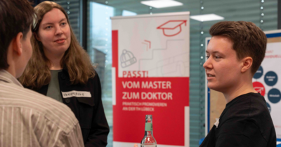 Promovierende im Austausch vor Infobanner „Vom Master zum Doktor“.