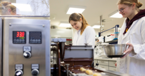 Zwei Frauen stehen vor einer kleinen Maschine, die Dinge mit Schokolade überzieht