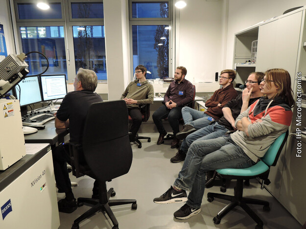 Ein Mitarbeiter des IHP zeigt den Studierenden wir Mikrochips mit einem fokussierten Ionenstrahl (FIB) unter einen Raster Elektronmikroskop aufgeschnitten und gegebenenfalls neue Verbindungen verlegt werden. Foto: IHP Microelectronics
