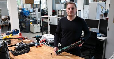 Ein Mann in Pulli steht vor einer Werkbank und hält eine Fahrradbatterie.
