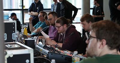 Menschen sitzen vor einem Mischpult und Monitoren.