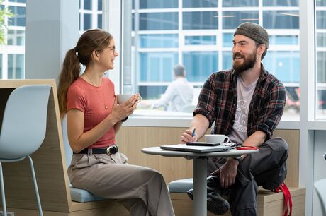 Lächelnder Mann und Frau im Gespräch an einem Tisch in heller Umgebung.
