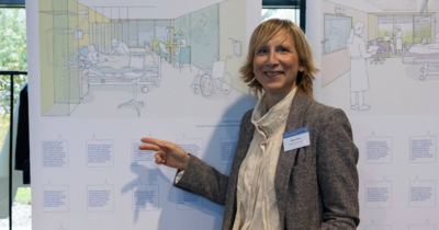 Eine Frau zeigt auf ein großes Plakat mit architektonischen Zeichnungen