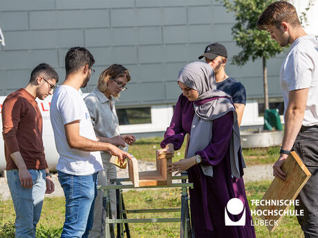 Auf diesem Bild sieht man sechs junge Menschen, die an einem Holzstück arbeiten