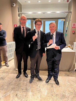 A man in a patterned tie holds an award, posing with two other men.