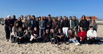 Eine Gruppe von Studierenden steht am Strand der Ostsee. 