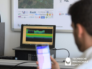 Station 5G Labor Ein Hinterkopf und ein Handy im vordergrund , ein Bildschirm im Vordergrund