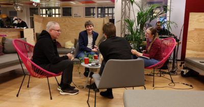 Vier Menschen sitzen auf gemütlichen Stühlen und machen einen Podcast