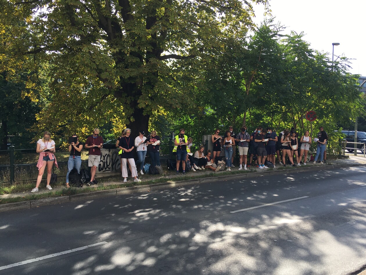 Studierendengruppe steht an einer Straße am Parkrand und zeichnet in Hefte.