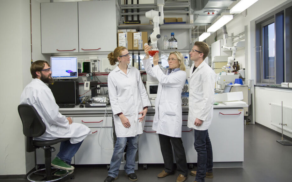 Studierende der Angewandten Chemie stehen im Labor und begutachten zusammen mit ihrer Professorin eine rote Flüssigkeit in einem Reagenzglas