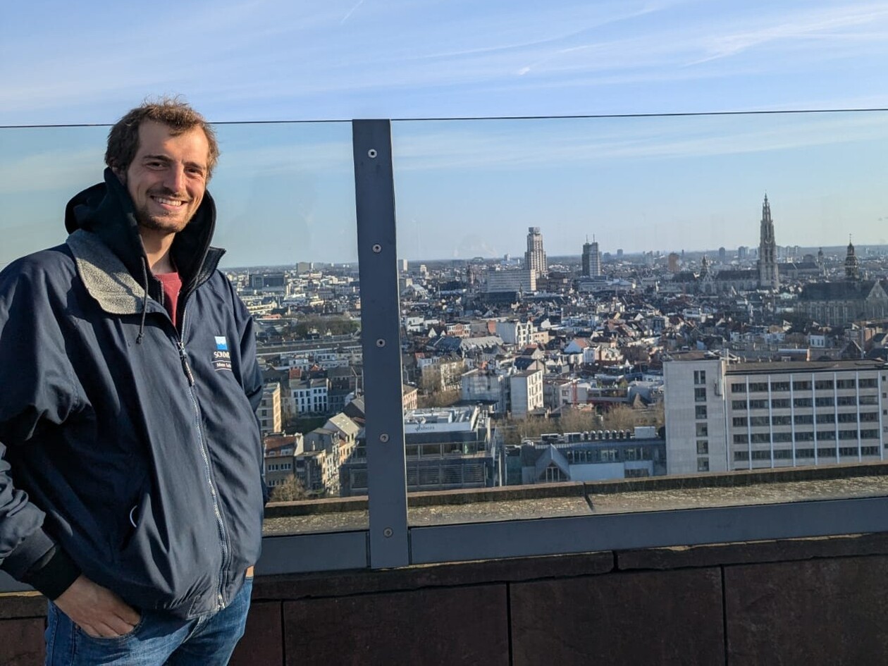 Student steht lächelnd auf einer Aussichtsplattform mit Blick über die Dächer von Antwerpen