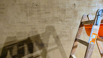 Das Bild zeigt eine Lehmwand und eine Leiter wirft einen Schatten auf die Wand.
