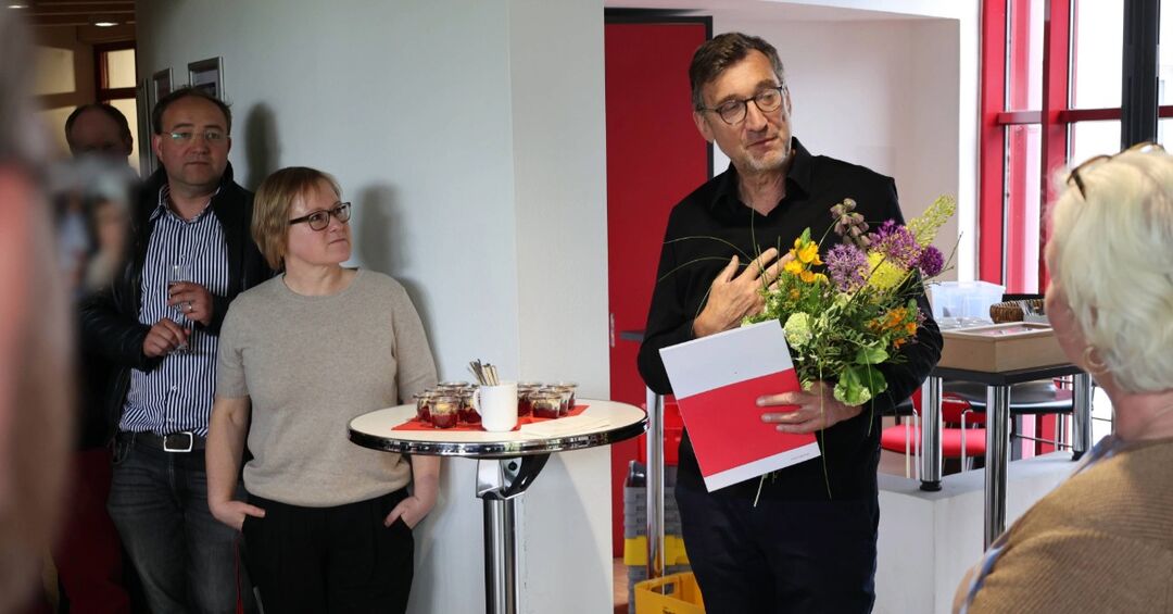 Ein Mann hält eine Mappe und Blumen in der Hand.